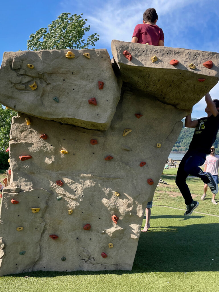 boy reaching the top of a climbing bolder