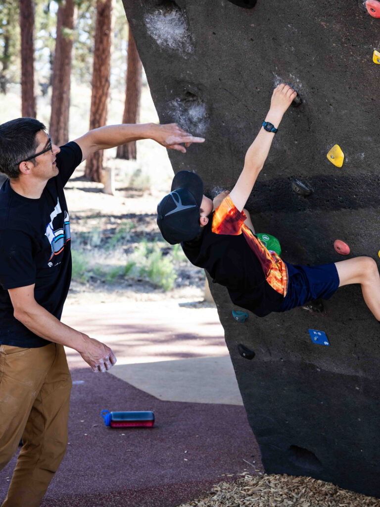 man assisting child climbing on a climbing bolder